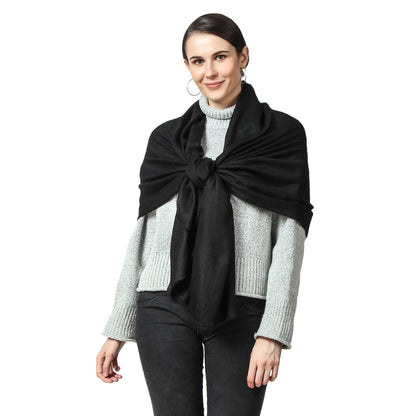 Image of a woman wearing a black cashmere scarf draped over her back and knotted in front. The knot is positioned slightly off-center and adds a stylish touch to the woman's outfit. The scarf is soft and luxurious-looking, and the black color adds to its classic and versatile style. The woman's expression is confident and composed, with a subtle smile on her face.